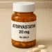 Realistic photo of an atorvastatin 20 mg prescription bottle on a kitchen counter with five oval white pills beside it.